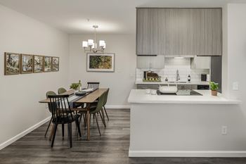 A kitchen with a dining table and chairs in the foreground and a kitchen island with a sink in the background.